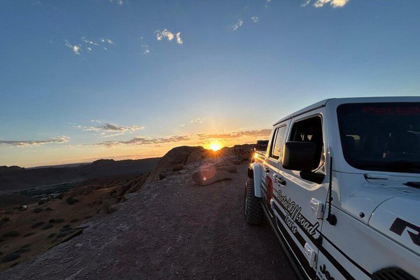 Un SUV blanco estacionado en un camino de tierra con un atardecer de fondo. 1