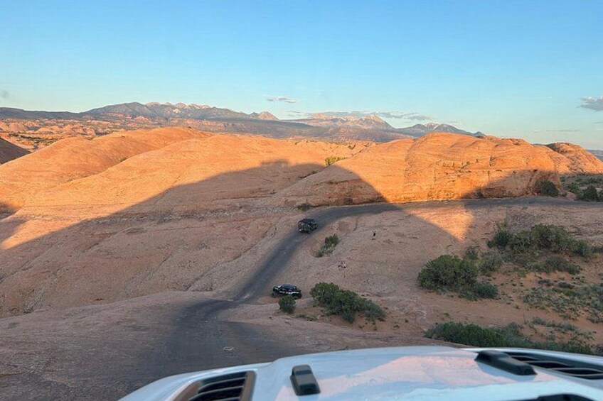 Paisaje desértico con un camino sinuoso, montañas a lo lejos y un vehículo en primer plano. 4