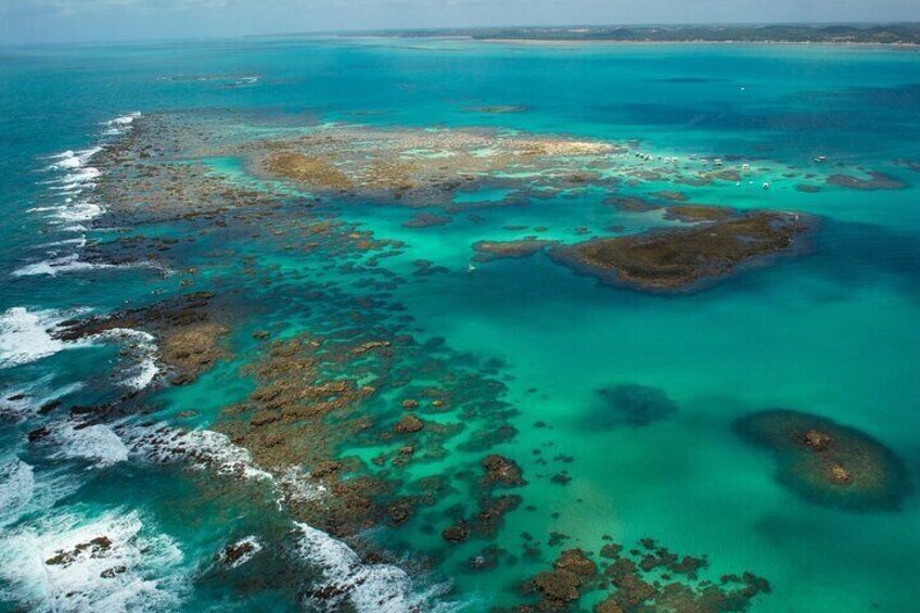 An aerial view of a coastal area with clear turquoise waters, rocky outcrops, and coral formations. 2