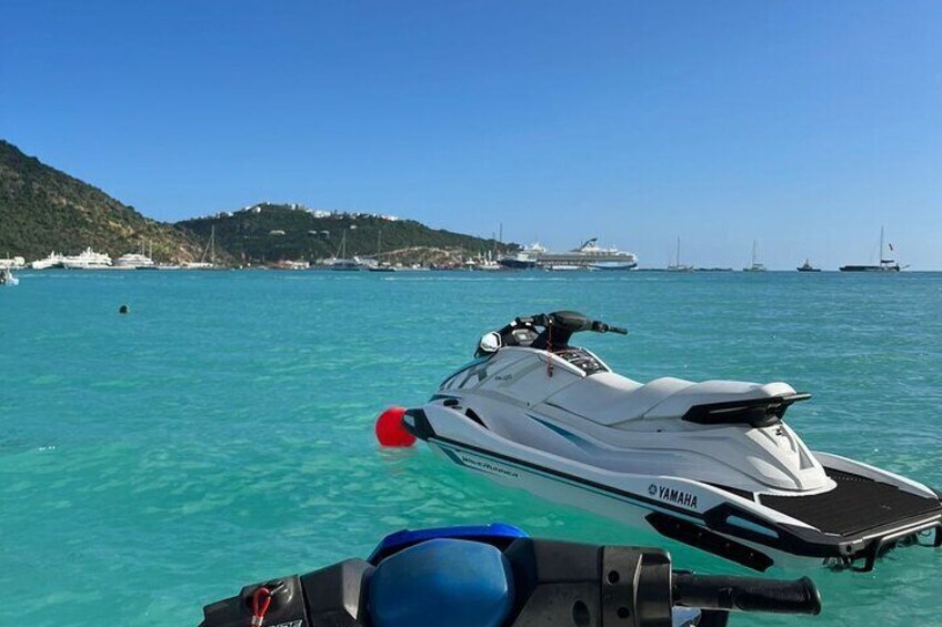 A white Yamaha jet ski on turquoise water with a boat in the background and a hilly landscape. 1