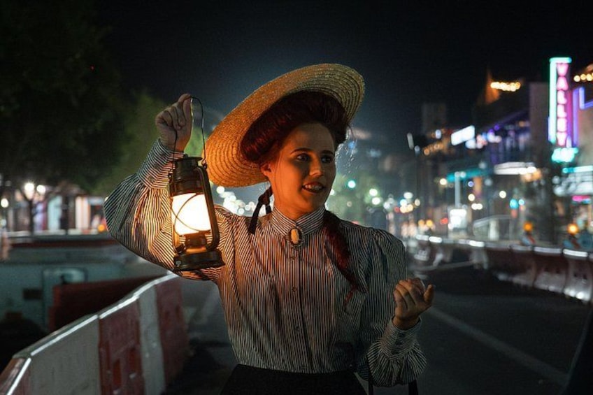 A person holding a lantern, wearing a striped shirt and a straw hat, standing on a bridge with city lights in the background. 3