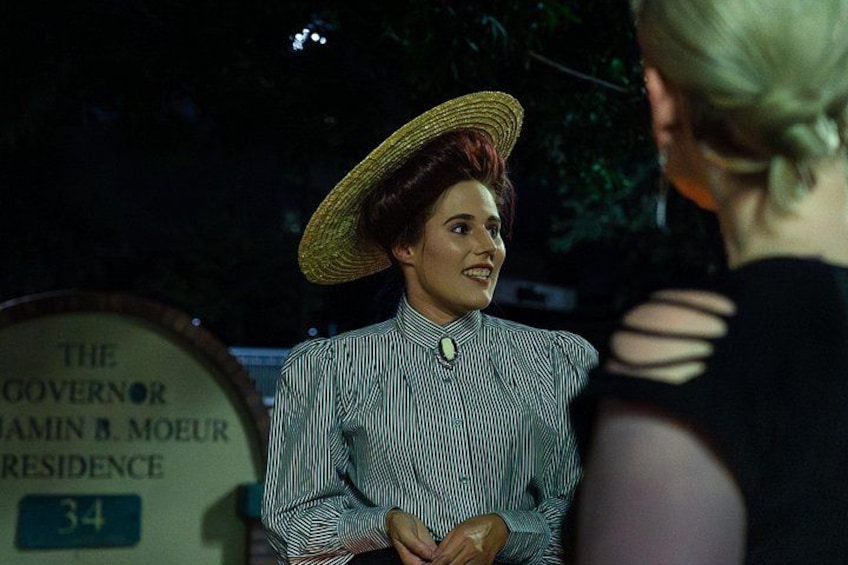 A person wearing a striped shirt and a straw hat, standing near a sign that reads 'The Governor's Residence.' 5