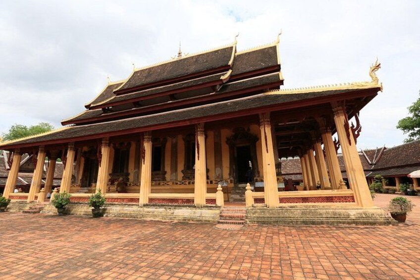 A traditional Thai temple with a multi-tiered roof, ornate columns, and a brick-paved courtyard. 5