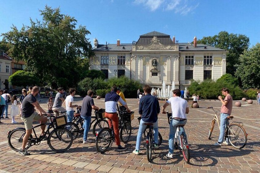 Een groep mensen die op fietsen rijdt in een binnenplaats, met een historisch gebouw op de achtergrond. 2