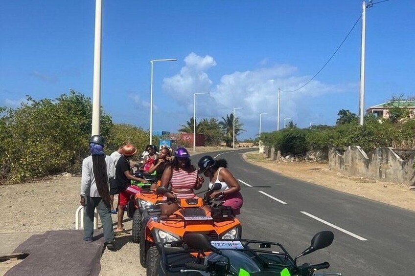 Un grupo de personas en un camino de tierra con vehículos, incluyendo un cuatrimoto naranja, y un cielo despejado. 5