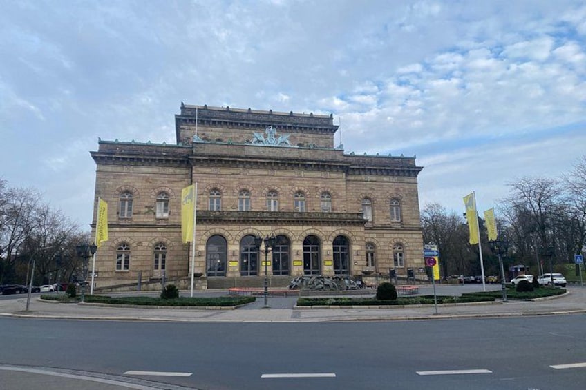 A historic building with arched windows and a central entrance, surrounded by a paved area with flags and a bicycle. 4