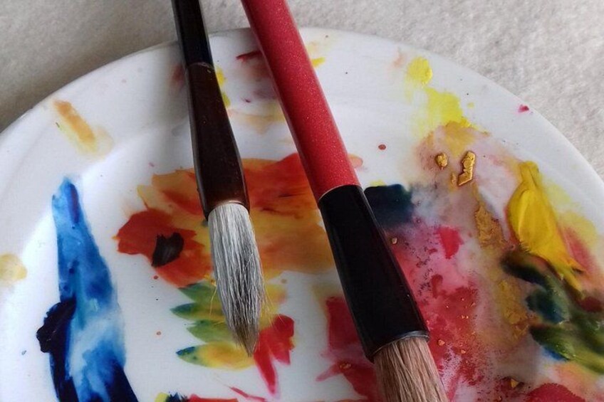 Un pinceau à manche rouge et à poils blancs, posé sur une assiette maculée d’éclaboussures de peinture colorée. 2