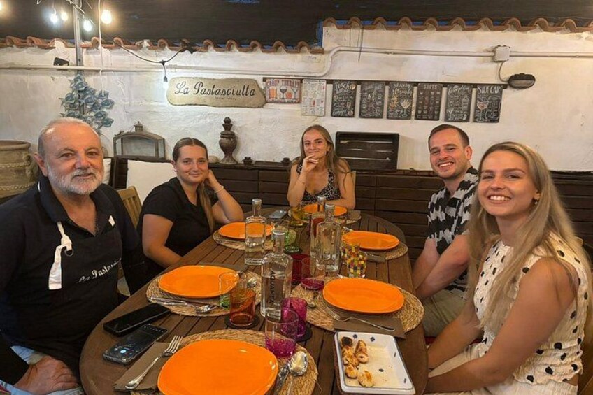 A group of people dining at a restaurant with orange plates and a sign reading 'La Pastasciutta.' 2