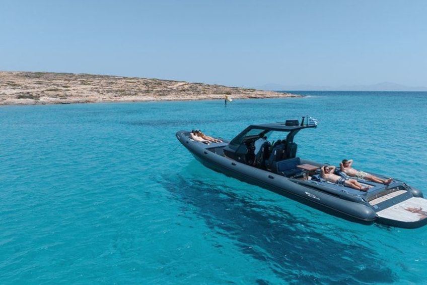 Ein kleines Schlauchboot auf klarem, blauem Wasser mit einer felsigen Küstenlinie im Hintergrund. 1