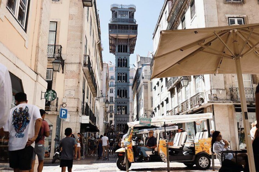 A narrow street with pedestrians, a parked tuk-tuk, and historic buildings. 3