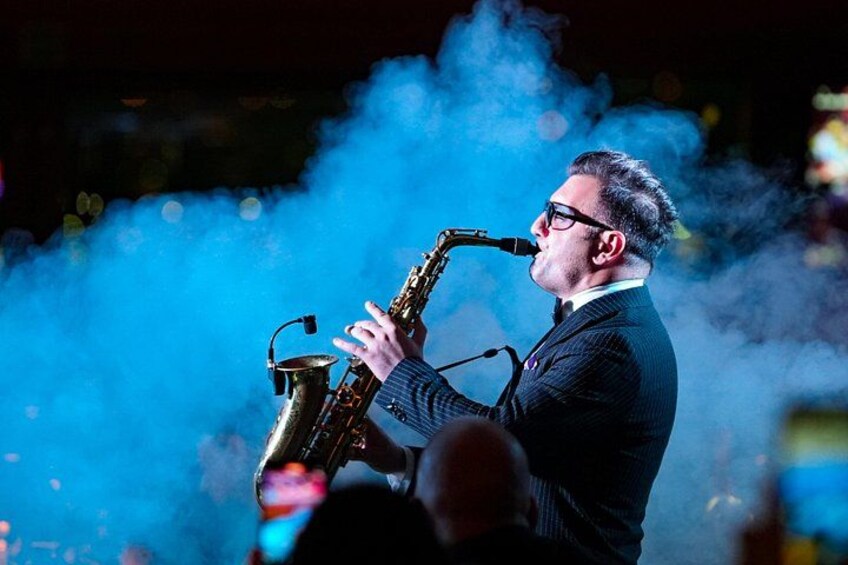 A person playing a saxophone on stage with blue smoke effects. 5