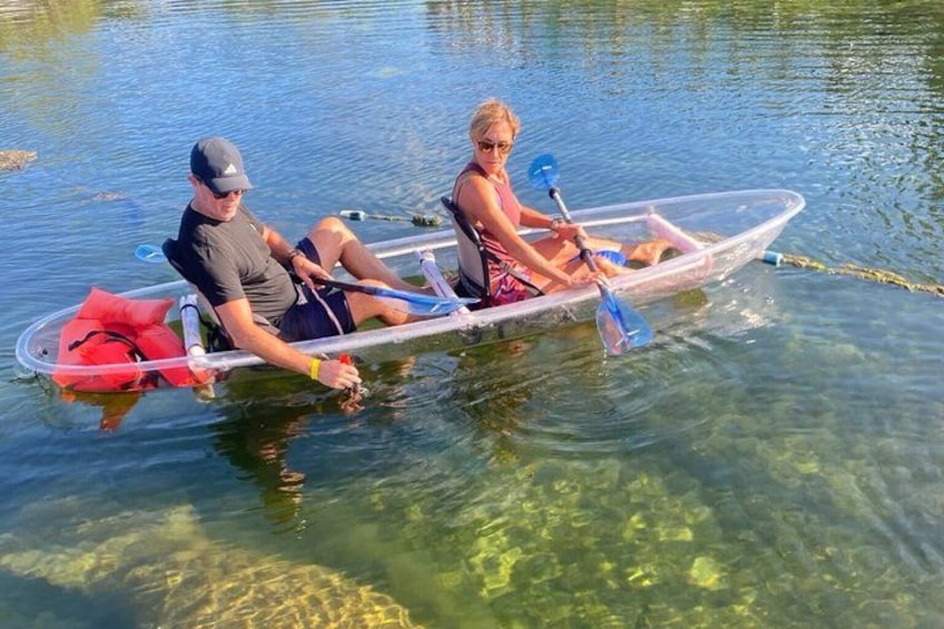 Two people in a transparent boat on a calm body of water. 3