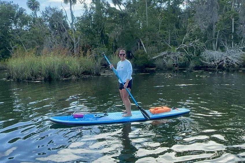 A person standing on a paddleboard in a body of water, surrounded by greenery. 3