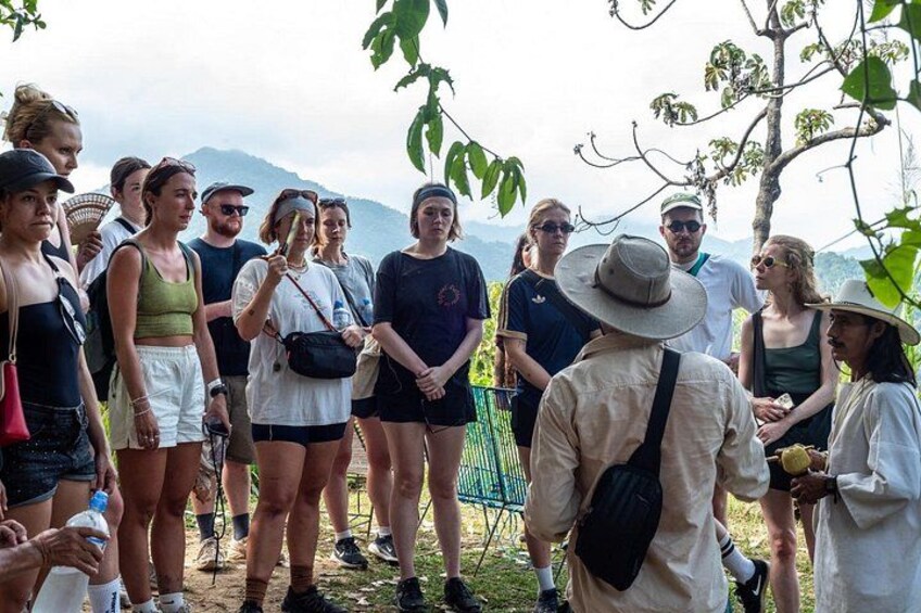 Un grupo de personas al aire libre, algunas de pie y otras sentadas, con árboles y montañas de fondo. 2