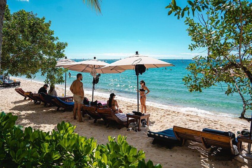 A beach with sun loungers, umbrellas, and people relaxing by the water. 5