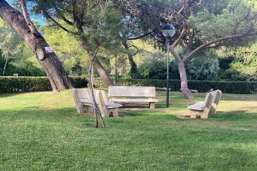 A park with a wooden bench, two stone chairs, and a lamppost. 4