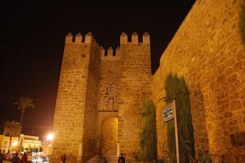 Une entrée de château en pierre, illuminée la nuit, avec un panneau indicateur. 5