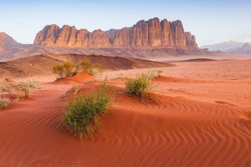 A desert landscape with red sand dunes and a prominent rock formation in the background. 5