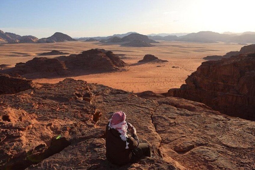 A person sitting on a rocky outcrop overlooking a vast desert landscape with distant mountains. 4