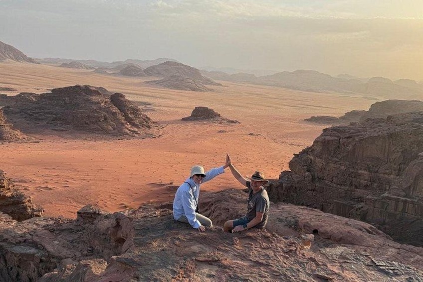 Two people sitting on a rocky outcrop with a desert landscape in the background. 2
