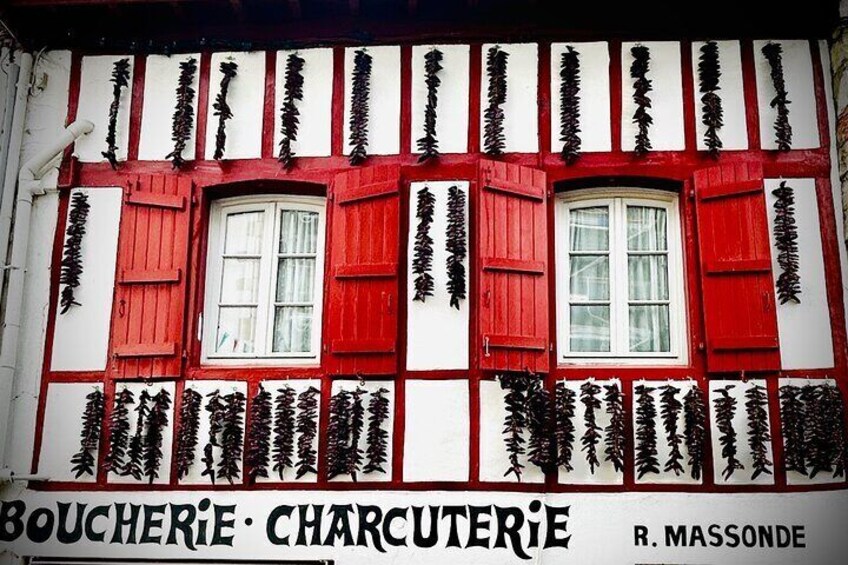Ein Gebäude mit roten Fensterläden und weißem Dekor, mit dem Text 'BOUCHERIE CHARCUTERIE' und 'R. MASSONDE'. 3