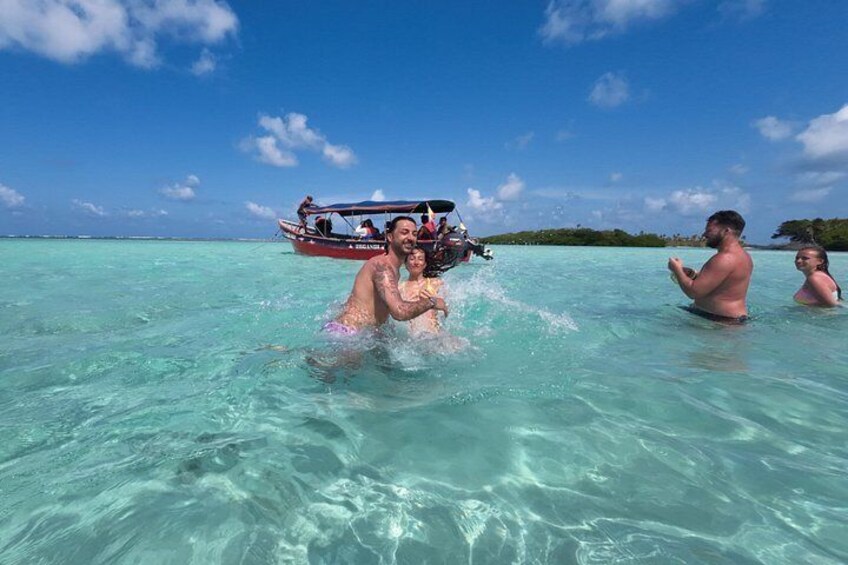 People in clear turquoise water, a boat with passengers, and a distant island. 4