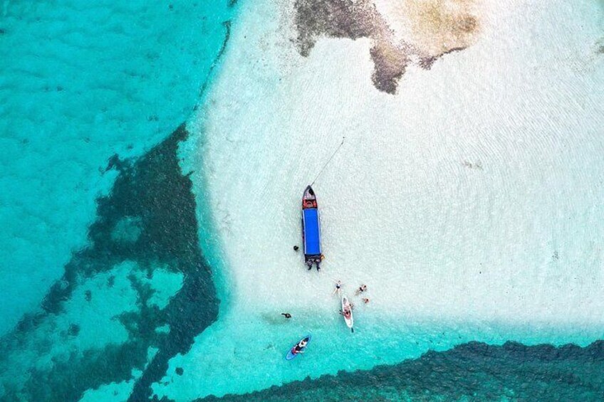 An aerial view of a beach with a boat anchored near the shore, surrounded by clear turquoise water. 3