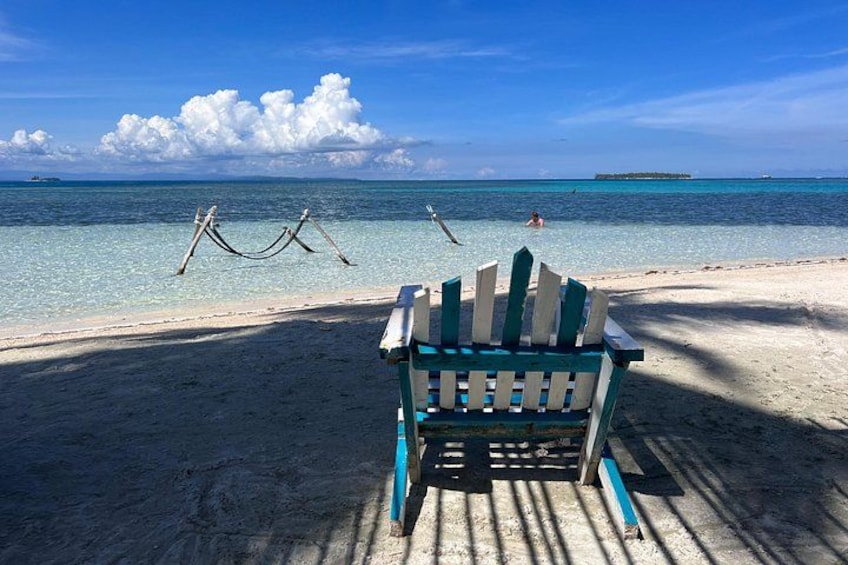 Una silla de playa en una orilla arenosa, con agua cristalina y una isla a lo lejos. 3