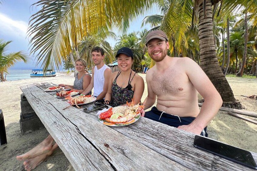 Een houten tafel met borden eten, met palmbomen en een strand op de achtergrond. 2