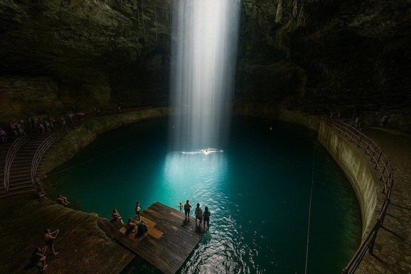 Una cascada dentro de una cueva con una poza en la base, rodeada por una pasarela y barandillas de madera. 5