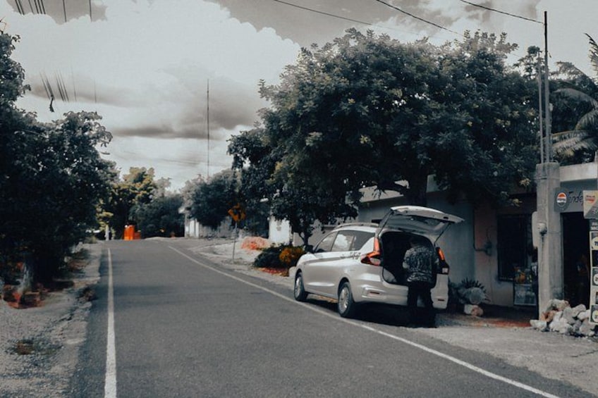 Una calle con un coche estacionado, árboles y un edificio con un cartel. 3