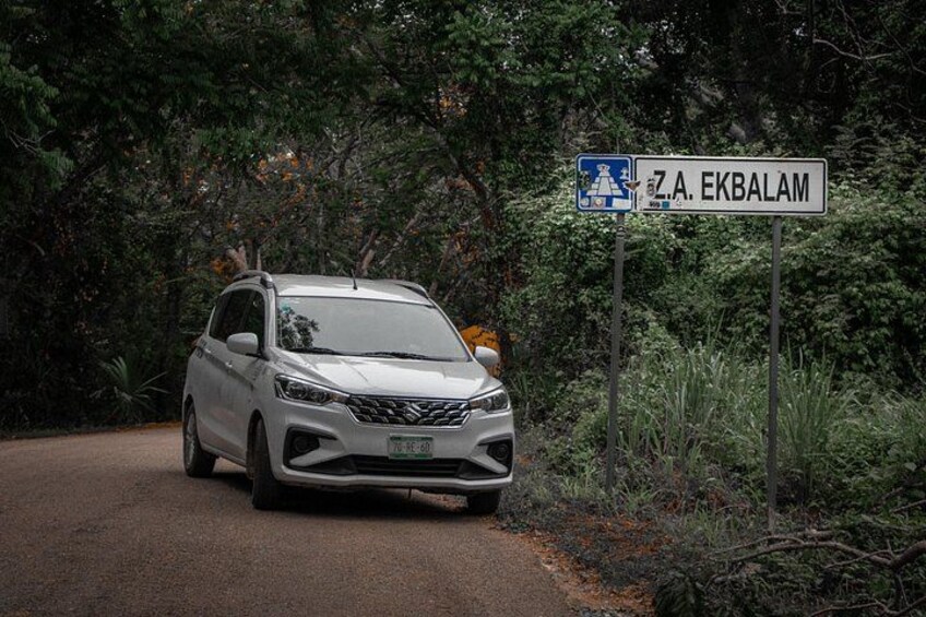 Un SUV blanco en una carretera con un letrero que dice 'Z.A. EKBALAM' y un símbolo de paso de peatones. 1
