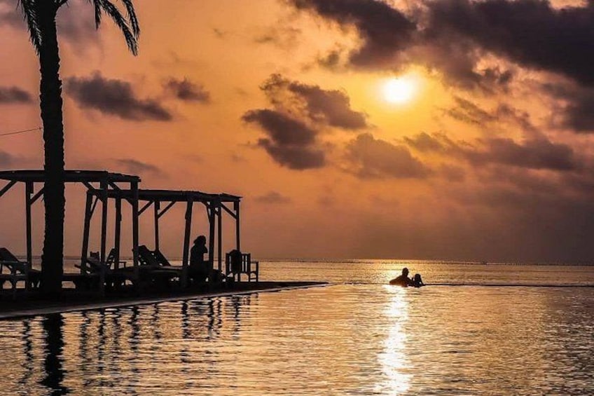 A sunset over a beach with a wooden structure and people in the water. 4