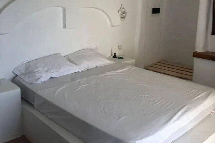 A white bed with a wooden headboard, a nightstand, and a small bedside table with a lamp. 3