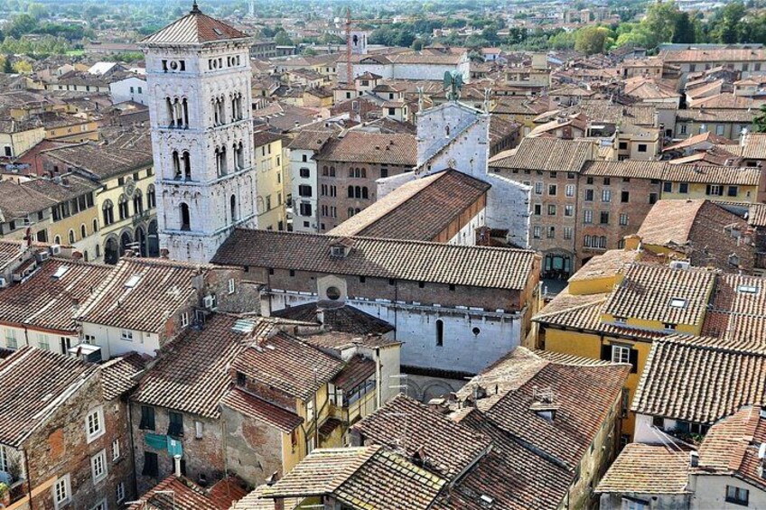 Un quartier urbain densément peuplé, caractérisé par des bâtiments historiques, une tour imposante et un mélange de toits recouverts de tuiles rouges. 2