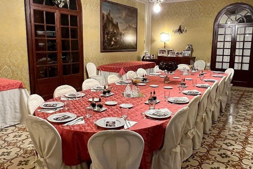 A dining room with a long table set for a meal, chairs, a chandelier, and a painting on the wall. 4