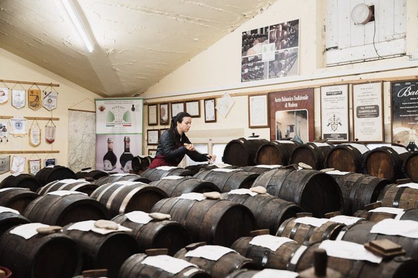A cellar with wooden barrels, a person inspecting them, and various framed certificates and posters on the walls. 3