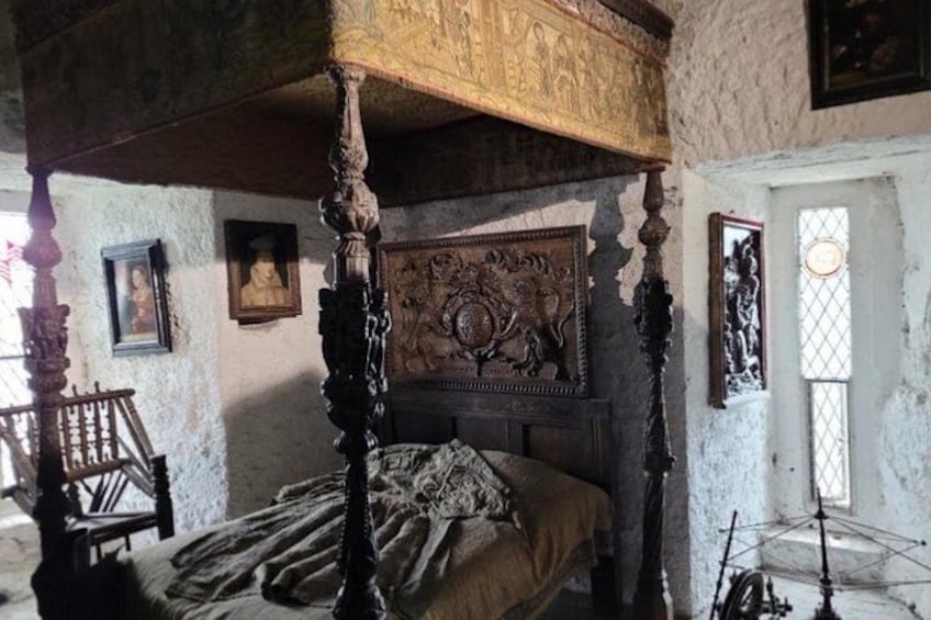 A bedroom with a four-poster bed, a wooden headboard with carvings, a stone wall, and a window with a decorative grille. 3