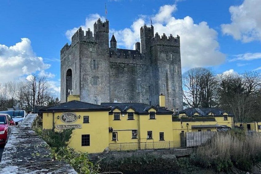 A castle with a yellow building in front, a clear sky, and a few cars parked nearby. 1