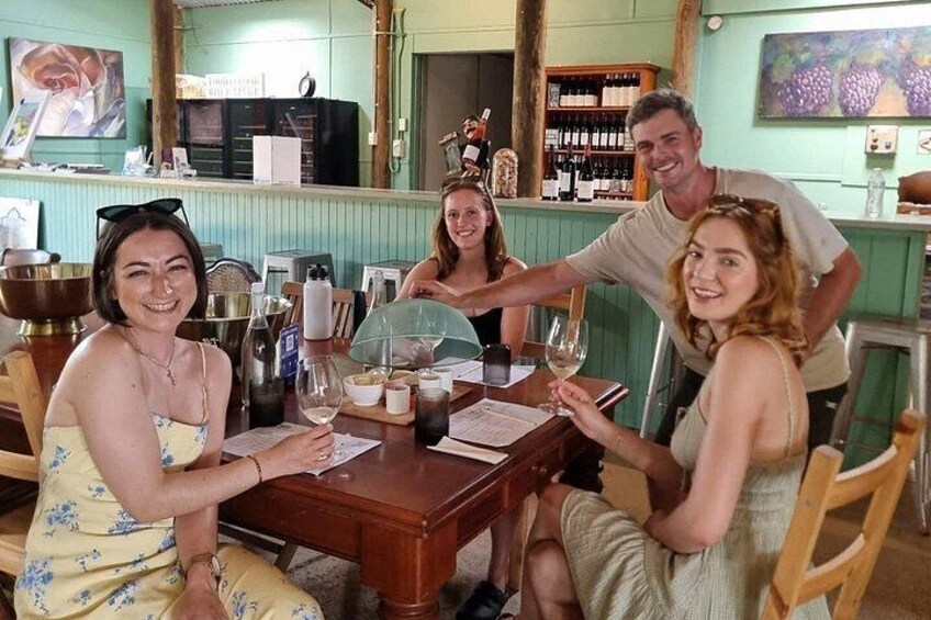 A group of people sitting around a table with wine glasses and bottles, in a restaurant with a green wall and wooden furniture. 4