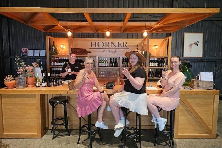 A bar with a sign that reads 'HORNER WINES' and three people sitting at the bar. 5
