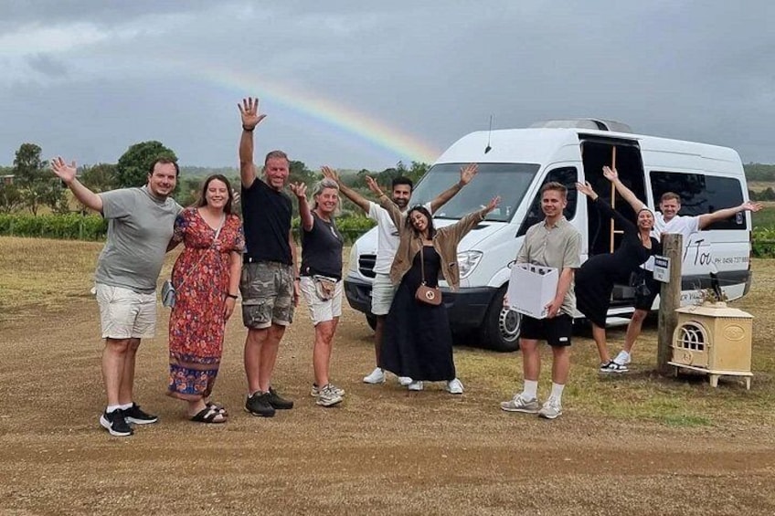 A group of people posing in front of a white van with a rainbow in the background. 3