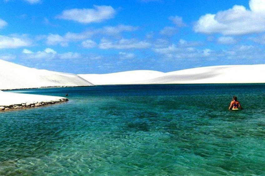 A person in a kayak on clear turquoise water with white sand dunes in the background. 2