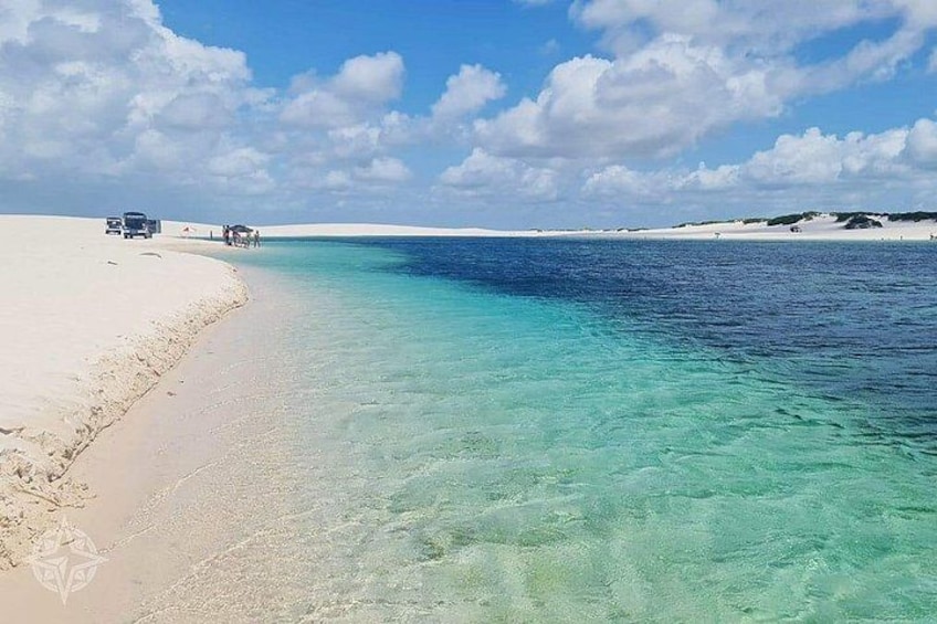 A beach with clear turquoise water, a sandy shore, and a few vehicles. 3