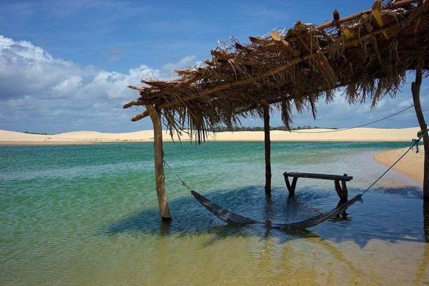 A hammock under a thatched roof by a calm sea with clear skies. 1