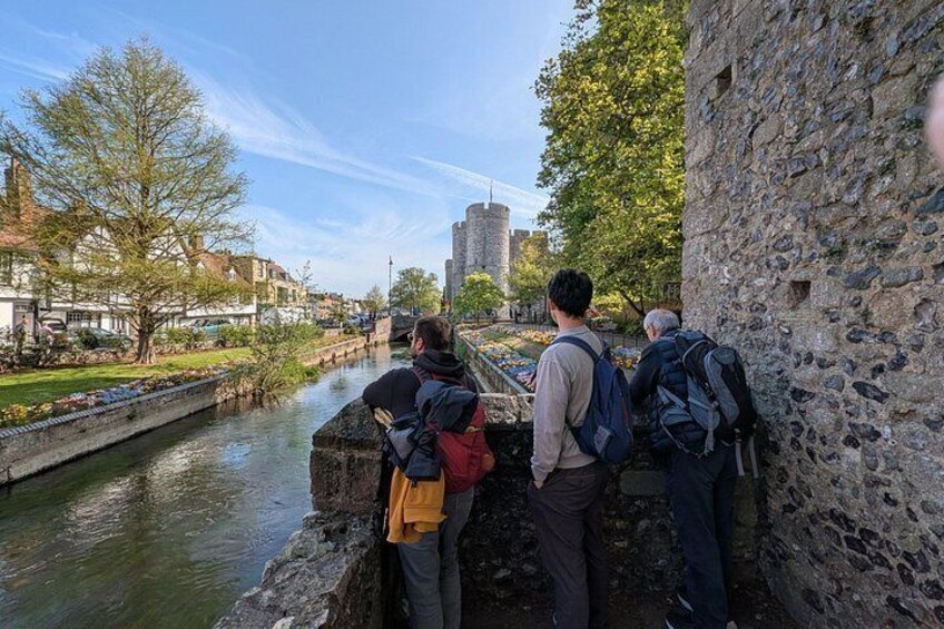 A group of people standing by a river, overlooking a cityscape with buildings and a bridge. 2
