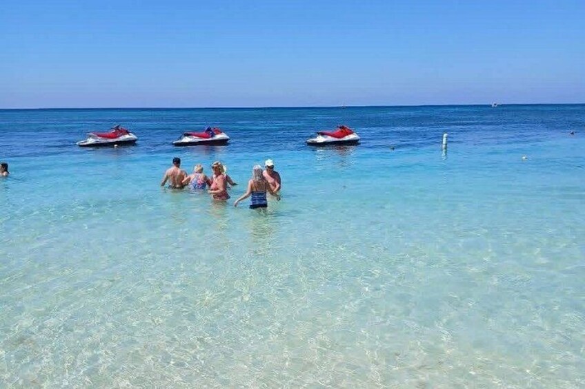A clear blue sea with people in the water and jet skis in the background. 2