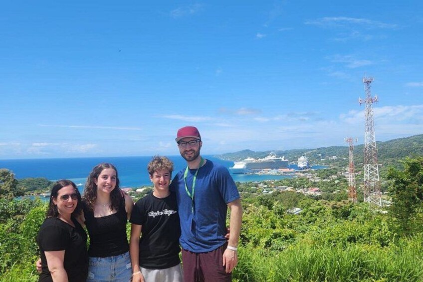 A group of people standing on a hill with a view of the ocean and a tall communication tower in the background. 5