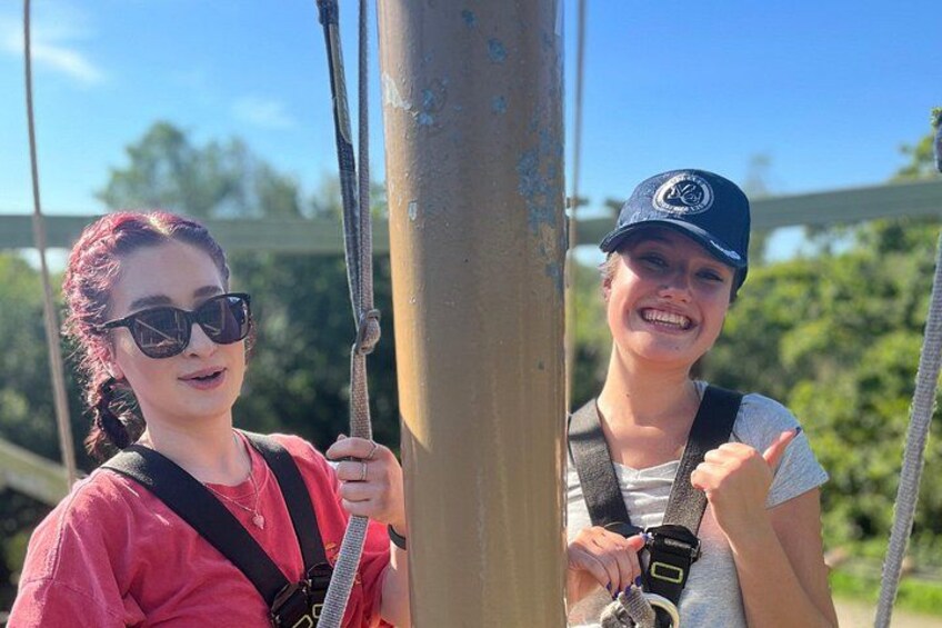 Two people on a zip line, wearing safety harnesses and helmets. 1