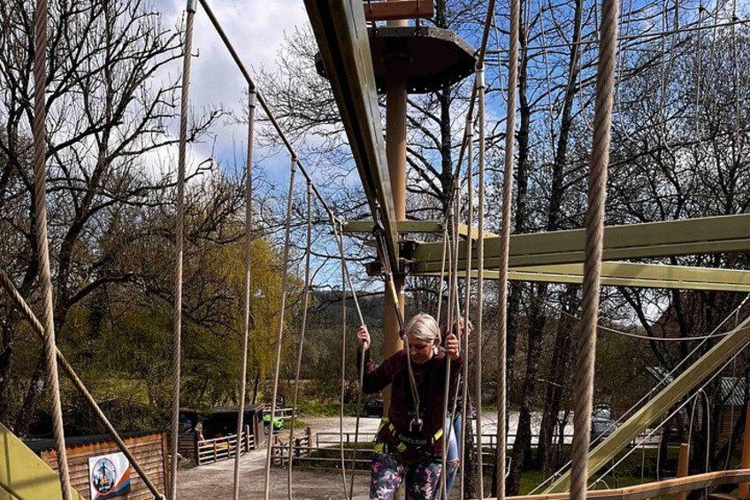 A person on a rope course with safety harness and ropes, surrounded by trees and a clear sky. 4